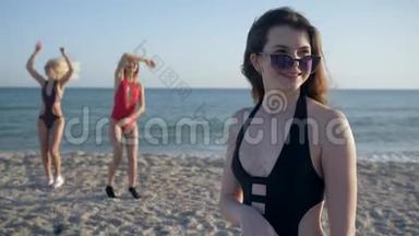 <strong>节</strong>日快乐，戴着墨镜、穿着<strong>泳装</strong>的笑脸女郎在沙滩上以欢快的女友为背景